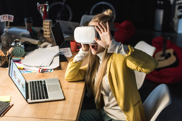 збуджена випадкова бізнес-леді жестикулює руками, маючи досвід віртуальної реальності за комп'ютерним столом в офісі
 - Фото, зображення