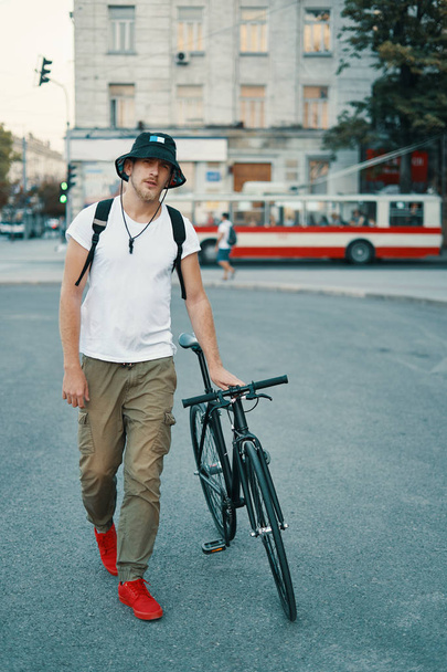 Stylish Man With Bicycle Going To Work On Street. Portrait Of Young Male In Casual Clothes With Backpack Walking On City Street With Stylish Bike. Red Sneakers. - Foto, immagini