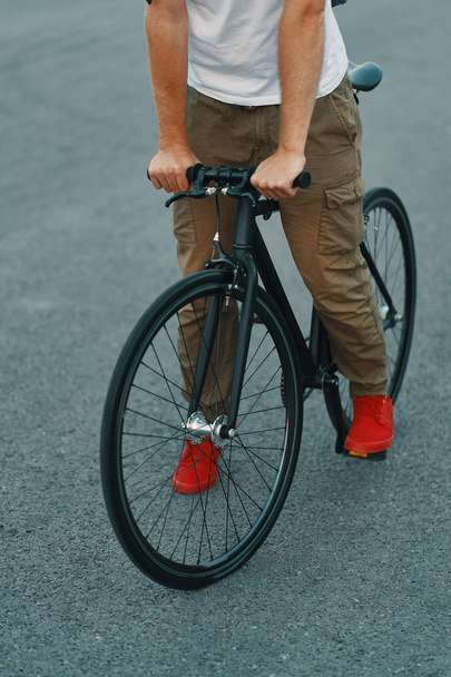 Lähikuva rento mies jalat ratsastus klassinen pyörä kaupungin harmaa tie yllään punaiset lenkkarit ja mukava housut. Kopioi tila
 - Valokuva, kuva