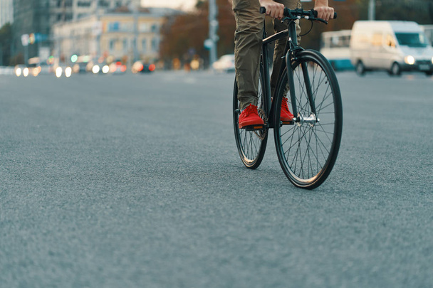 Close-up de pernas de homem casual andar de bicicleta clássica na estrada cinza da cidade vestindo tênis vermelhos e calças confortáveis. Espaço de cópia
 - Foto, Imagem