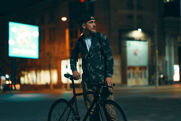 Pyöräilijät seisoo tiellä syrjään hänen klassinen pyörä katsellessaan valaistu kaupunki
 - Valokuva, kuva