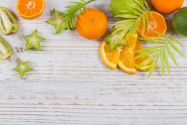 Hojas de palma verde y rodajas tropicales frescas de frutas sobre una mesa de madera blanca. Naranjas jugosas, mandarinas, limas, carambolas. Fondo de fruta de verano. Plano, vista superior, espacio para copiar
 - Foto, Imagen