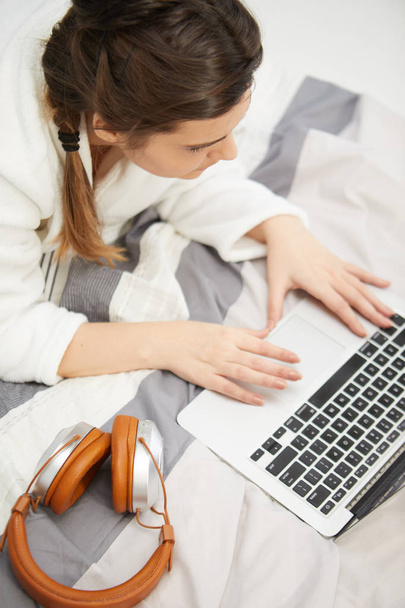 Jeune femme travaillant avec un ordinateur portable couché sur le lit dans la chambre lumineuse et confortable à la maison
 - Photo, image