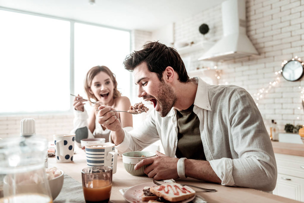 bärtiger gutaussehender positiver Mann im weißen Hemd, der Salat zum Frühstück isst - Foto, Bild
