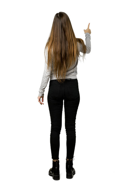 Полнометражный снимок молодой девушки, указывающей назад указательным пальцем на изолированном белом фоне
 - Фото, изображение