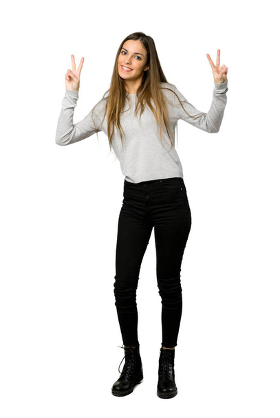 Повнометражний знімок молодої дівчини, яка посміхається і показує знак перемоги обома руками на ізольованому білому тлі
 - Фото, зображення