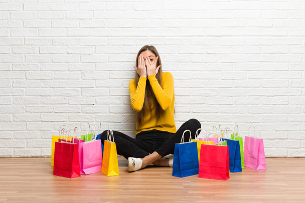 Chica joven con un montón de bolsas de compras que cubren los ojos por las manos y mirando a través de los dedos
 - Foto, Imagen