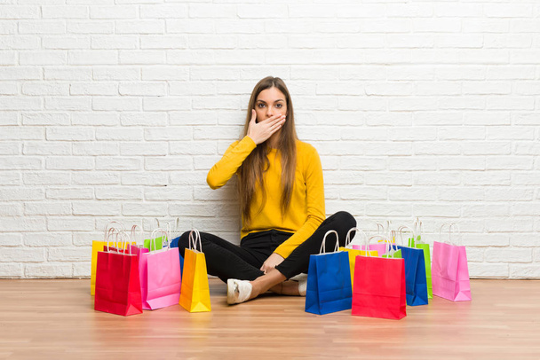 Mladá dívka s množstvím nákupních tašek pokrývající ústa rukama říkám něco nepatřičného - Fotografie, Obrázek