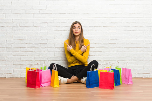 Young girl with lot of shopping bags pointing to the laterals having doubts - Photo, Image