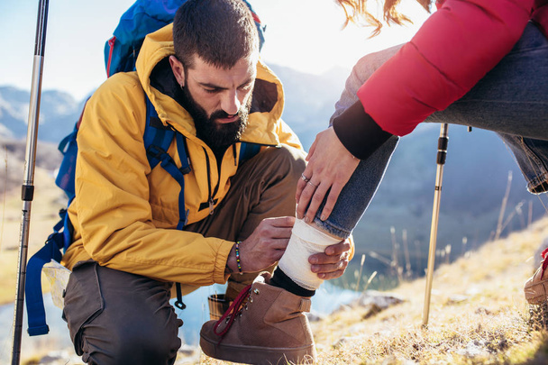 A woman has sprained her ankle while hiking, her friend uses the first aid kit to tend to the injury - 写真・画像