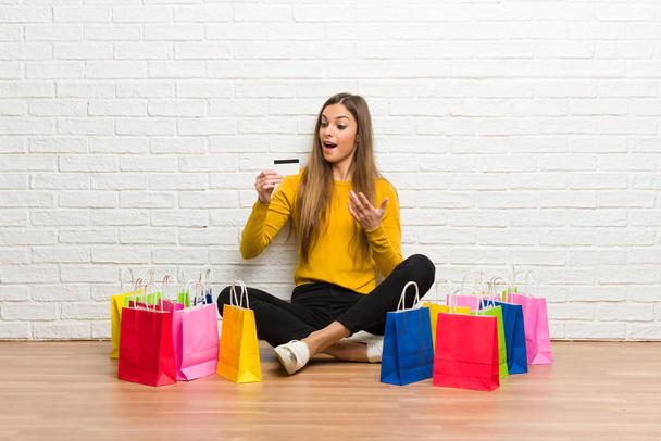 Chica joven con un montón de bolsas de compras con una tarjeta de crédito y sorprendido
 - Foto, imagen