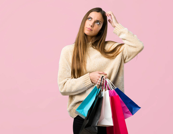 Chica joven con bolsas de compras que tienen dudas mientras se rasca la cabeza en el fondo rosa aislado
 - Foto, Imagen