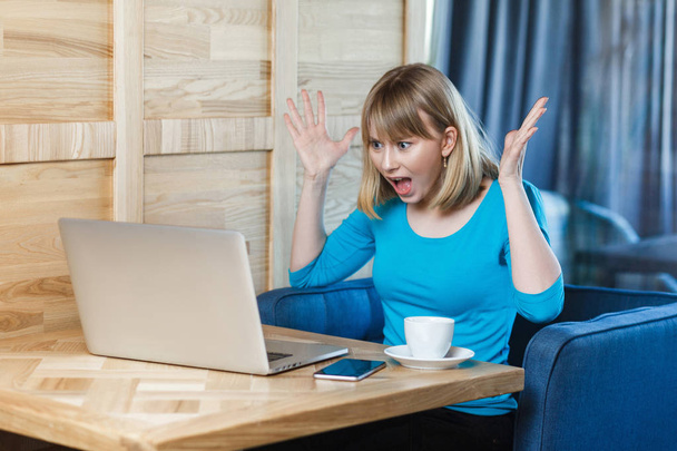 aggressive unglückliche Freiberuflerin in blauer Bluse, die schlechte Laune hat, während sie Arbeiter durch Laptop-Webcam mit erhobenen Armen im Café ermahnt  - Foto, Bild