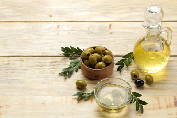green olives with leaves in a wooden bowl with olive oil on a natural wooden table. space for text - Φωτογραφία, εικόνα