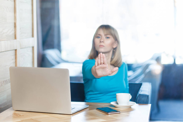mujer infeliz agresiva freelancer en blusa azul con mal humor y mostrando gesto de parada con la palma mientras está sentado en la cafetería
  - Foto, imagen