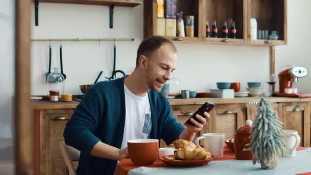 Man using phone while having cup of coffee in kitchen at home 4k - Materiał filmowy, wideo