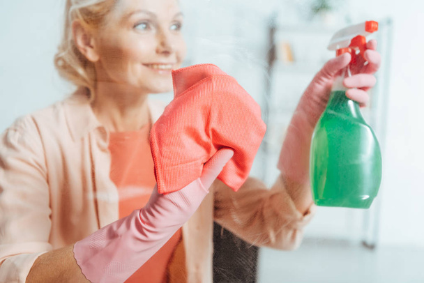 Carefree senior woman in pink rubber gloves cleaning window - Foto, Imagen