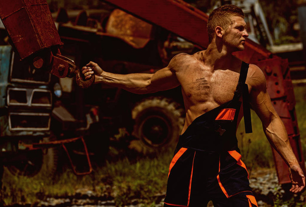 Muscle concept. Muscle man in working uniform pull heavy iron crane. Worker with muscle chest and arm biceps on construction site. Muscle activity - Φωτογραφία, εικόνα