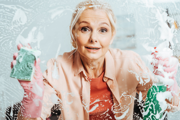 Surpris femme âgée fenêtre de nettoyage avec spray et éponge
 - Photo, image