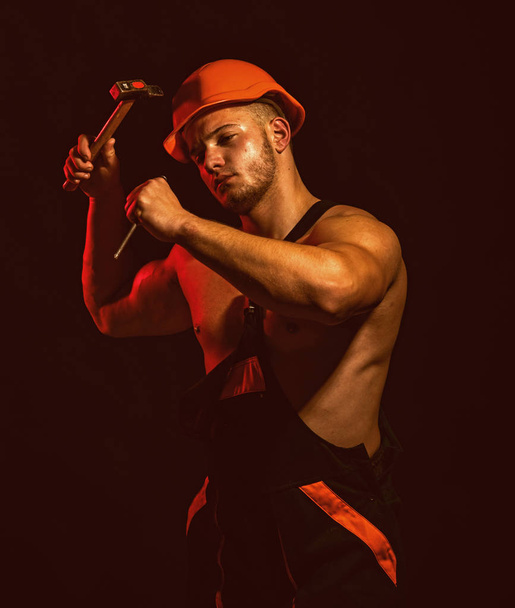A site is also under construction. Construction worker hammer a nail. Man work with hammer. Hard worker use muscular strength. Muscular man builder at work under construction - Фото, изображение