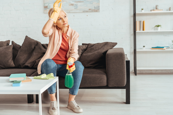 Tired woman with cleaning spray sitting on sofa - Photo, Image