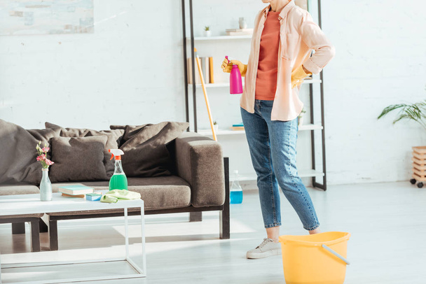Partial view of woman in jeans posing with cleaning supplies - Foto, imagen