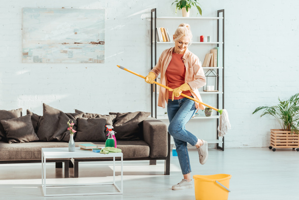 Superbe femme âgée dansant tout en nettoyant le sol dans le salon
 - Photo, image