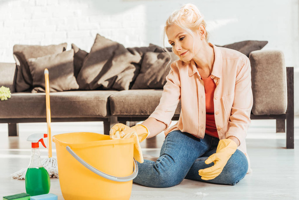 Mujer mayor cansada en guantes de goma amarilla limpiando piso
 - Foto, imagen
