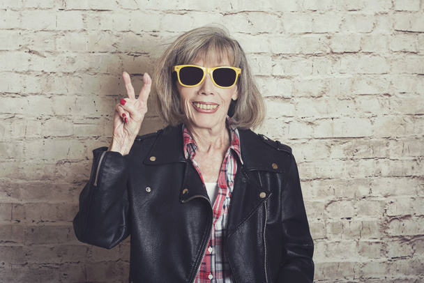 lachende senior vrouw met zonnebril op baksteen achtergrond - Foto, afbeelding