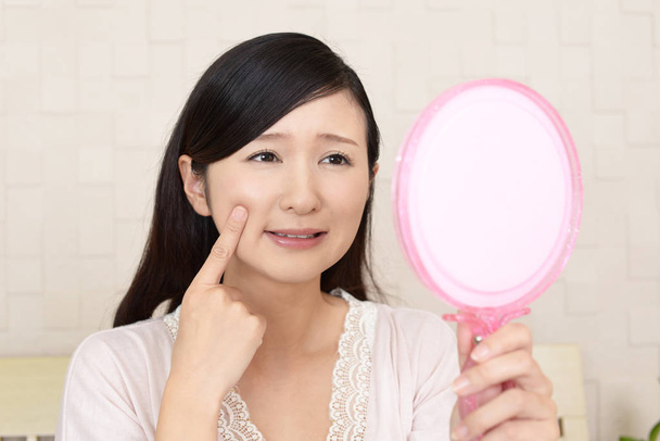 Asian woman looking at her face in mirror - Photo, Image