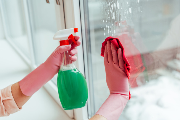 Vue partielle de la femme en gants roses nettoyage fenêtre avec spray et chiffon
 - Photo, image