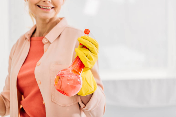 Vista recortada de la mujer sonriente en guante amarillo sosteniendo la botella de spray
 - Foto, imagen