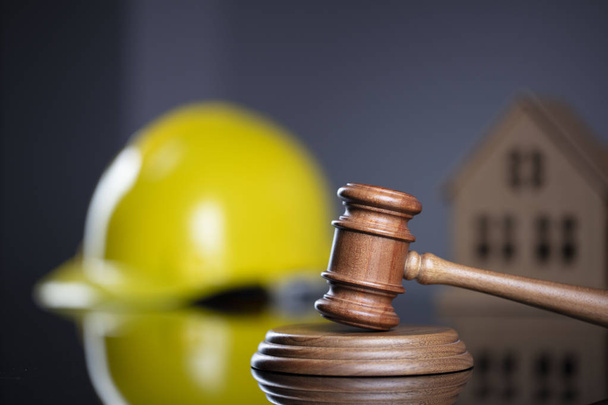Концепция строительного права. Деревянный молоток на сером фоне с моделью дома и желтым капотом
. - Фото, изображение