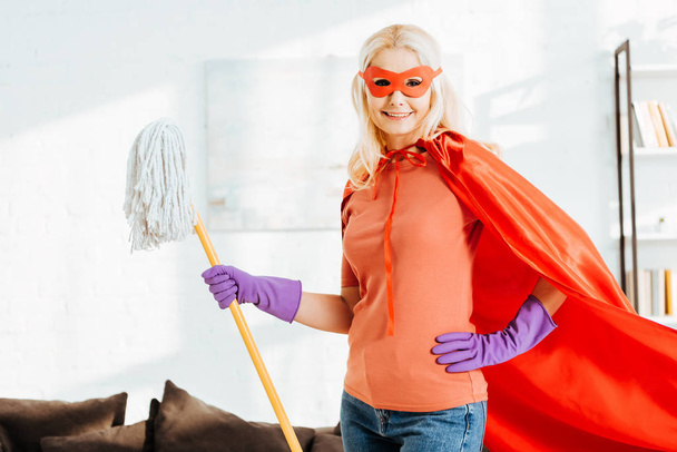 Senior woman with mop laughing while posing in superhero costume  - Foto, Bild