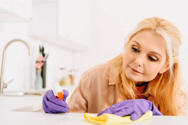 Mulher sênior em luvas roxas limpeza cozinha fogão
 - Foto, Imagem