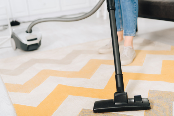 Partial view of woman cleaning striped carpet with vacuum cleaner - Photo, Image