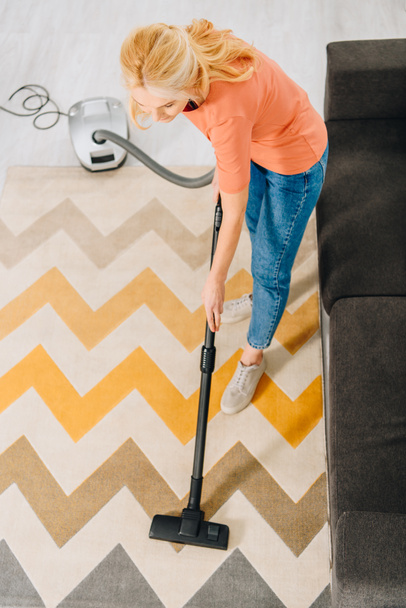 Vue du dessus de la femme en jeans nettoyage tapis avec aspirateur
 - Photo, image