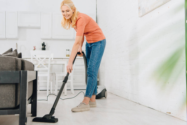 Happy senior woman cleaning floor with vacuum cleaner - Foto, Imagem