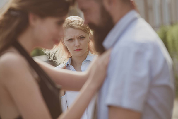 A jealous wife. Unhappy girl feeling jealous. Romantic couple of man and woman dating. Bearded man cheating his girlfriend with another woman. Jealous woman look at couple in love on street - 写真・画像