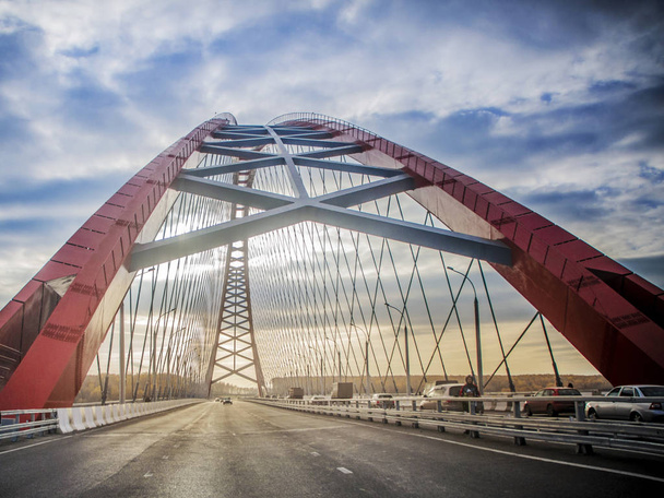 Beautiful background and view, landscape and panorama of the modern cable-stayed arched type, the red bridge and the road with cars against the blue sky with clouds. - Photo, image