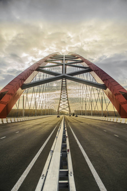 Beautiful background and view, landscape and panorama of the modern cable-stayed arched type, the red bridge and the road with cars against the blue sky with clouds. - Foto, Bild