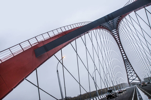 Beautiful background and view, landscape and panorama of the modern cable-stayed arched type, the red bridge and the road with cars against the blue sky with clouds. - Фото, изображение