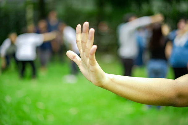 donna solleva la mano e mostrare cinque dita della mano in giardino, sfocare un sacco di persone in background
. - Foto, immagini