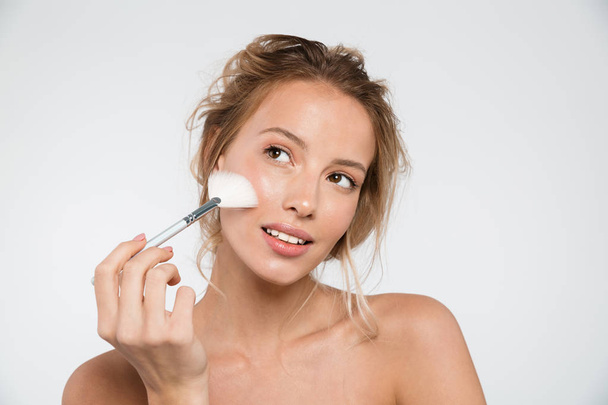 Image of a beautiful young woman posing isolated over white wall background holding makeup brushes. - Photo, image