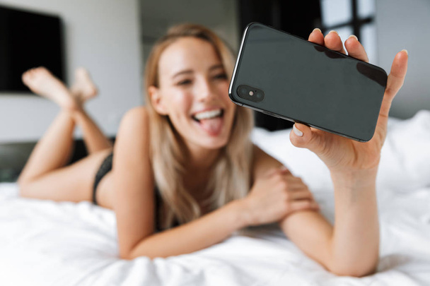 Beautiful young woman in lingerie underwear at morning in bed at home take a selfie by mobile phone. - Foto, immagini