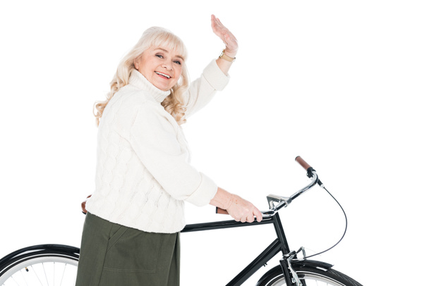 cheerful senior woman waving hand near bicycle isolated on white - Zdjęcie, obraz