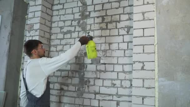строитель увлажняет кирпичную стену с помощью распылителя воды
 - Кадры, видео