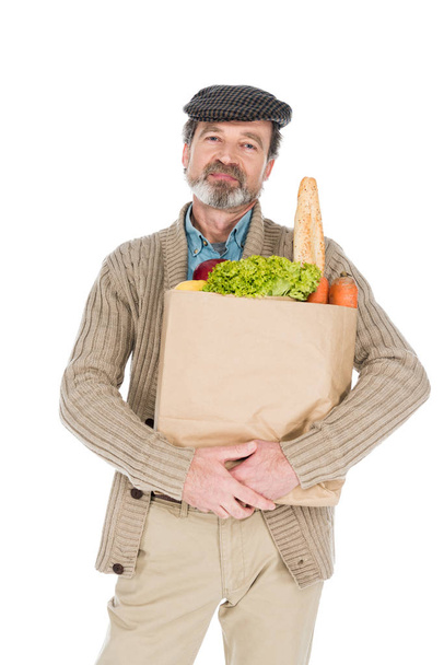 cheerful senior man holding paper bag with groceries isolated on white - Foto, Imagem