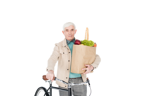 retired man holding paper bag with products and bike isolated on white - Foto, Imagen