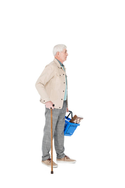 hombre retirado sosteniendo cesta de la compra y de pie con bastón aislado en blanco
 - Foto, Imagen